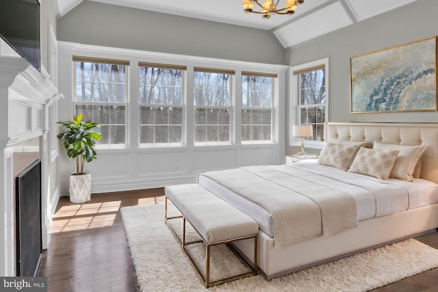 bedroom with dark wood finished floors, vaulted ceiling, a fireplace, and an inviting chandelier