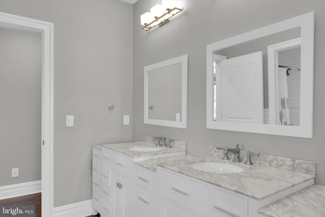 bathroom with baseboards, double vanity, a sink, and wood finished floors