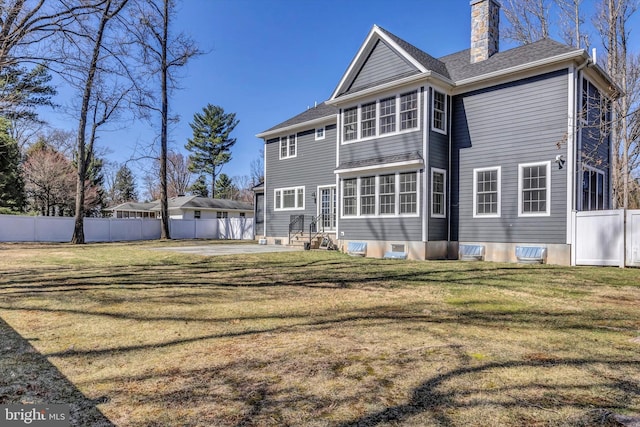back of house featuring fence, a patio, entry steps, a yard, and a chimney