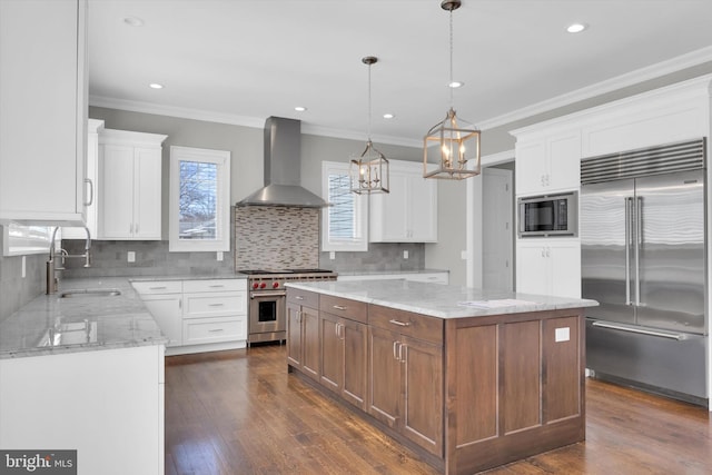 kitchen featuring a chandelier, dark wood finished floors, a sink, built in appliances, and wall chimney range hood