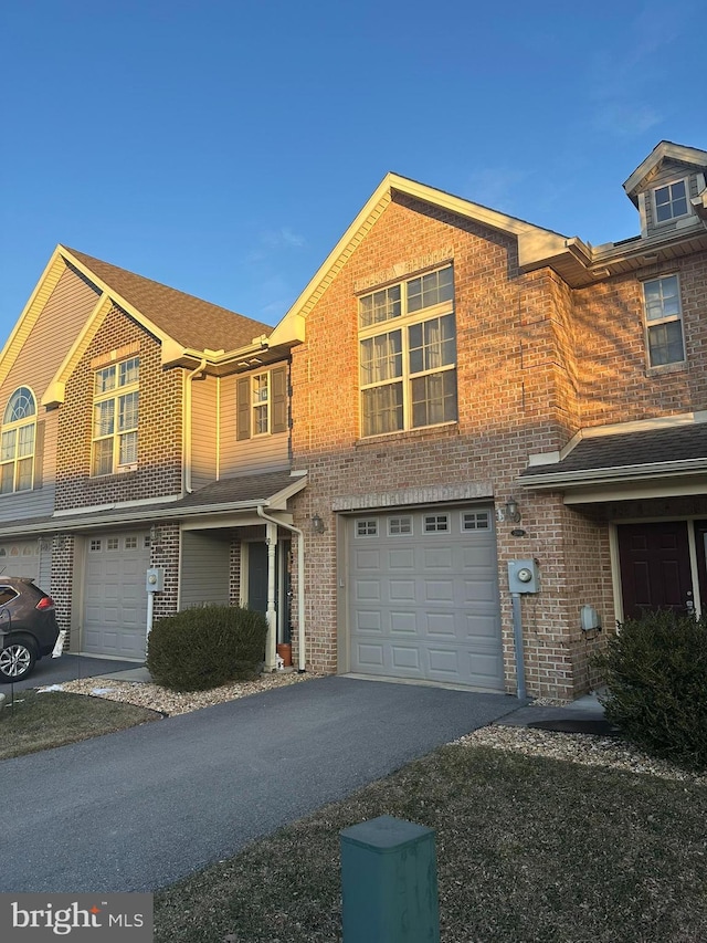 view of property featuring aphalt driveway, brick siding, and a garage