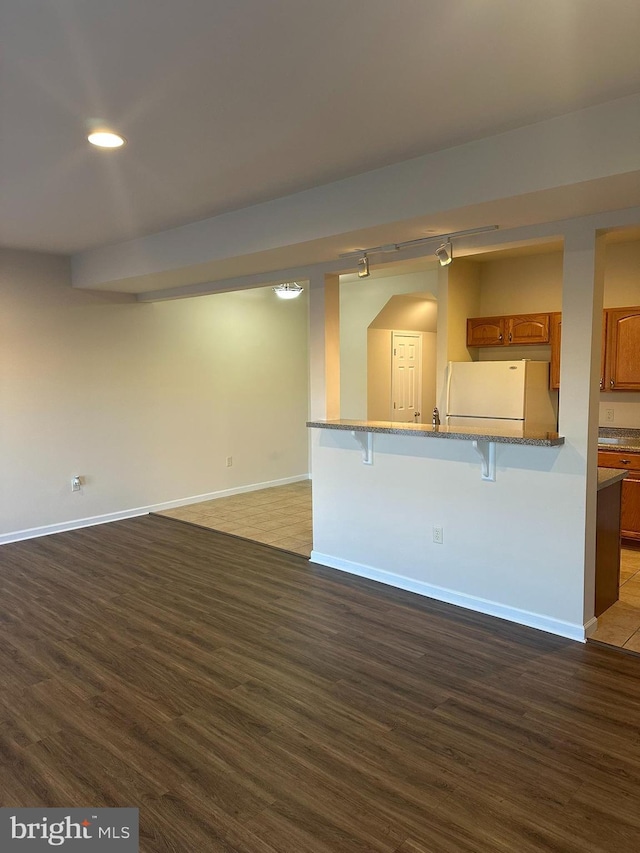 kitchen featuring a breakfast bar area, brown cabinetry, dark wood-style flooring, and freestanding refrigerator