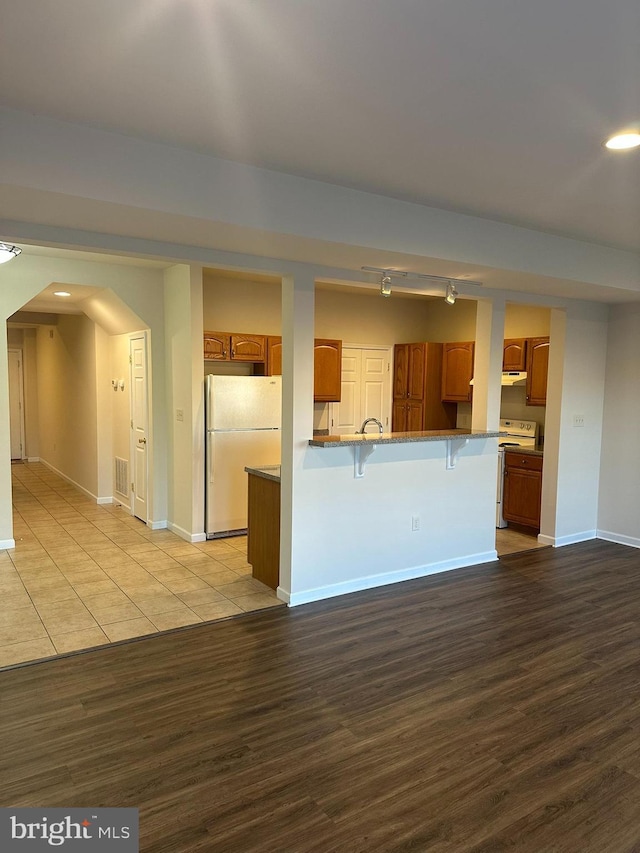 kitchen with white appliances, a breakfast bar area, light wood-style flooring, and brown cabinets