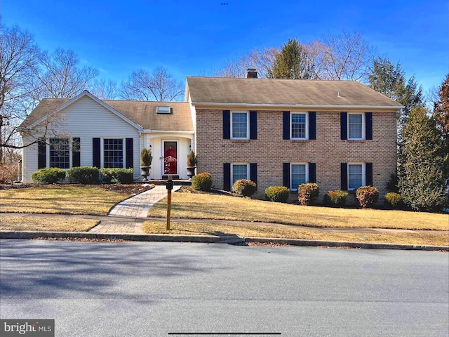 view of front of home with a front yard, a chimney, and brick siding