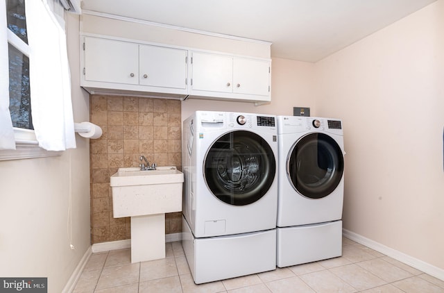 laundry room featuring cabinet space, light tile patterned flooring, a sink, washer and dryer, and baseboards