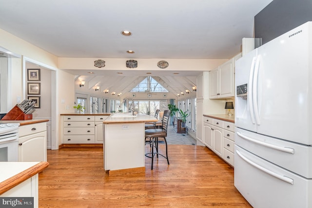 kitchen with white appliances, a sink, white cabinetry, light wood finished floors, and a kitchen bar