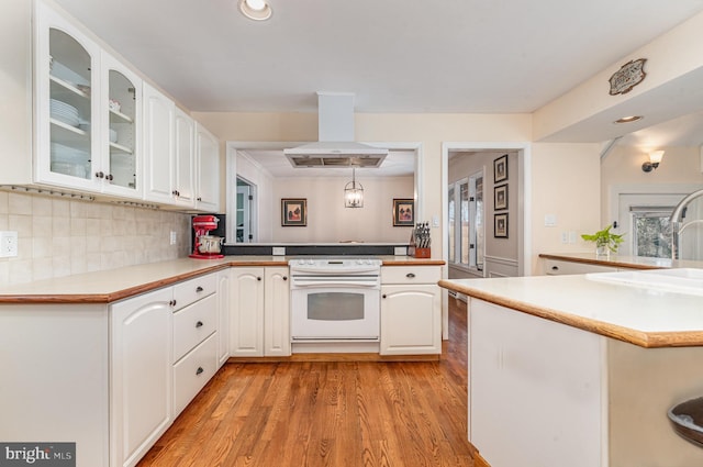 kitchen featuring island range hood, glass insert cabinets, a peninsula, white cabinetry, and white range with electric cooktop