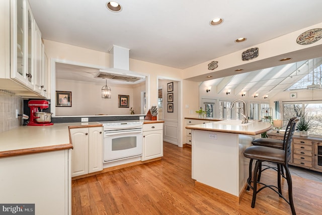 kitchen with a breakfast bar, light wood finished floors, white range with electric cooktop, white cabinetry, and extractor fan