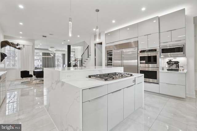 kitchen featuring a large island, marble finish floor, modern cabinets, decorative light fixtures, and built in appliances