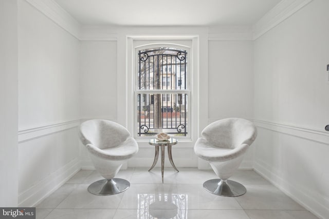 living area featuring tile patterned flooring, a decorative wall, wainscoting, and ornamental molding