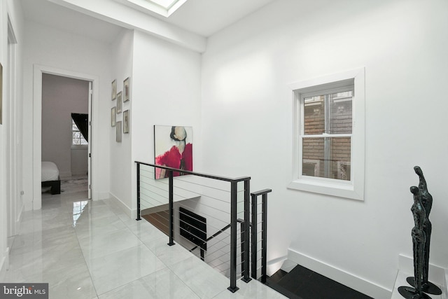 hallway featuring a skylight, an upstairs landing, and baseboards