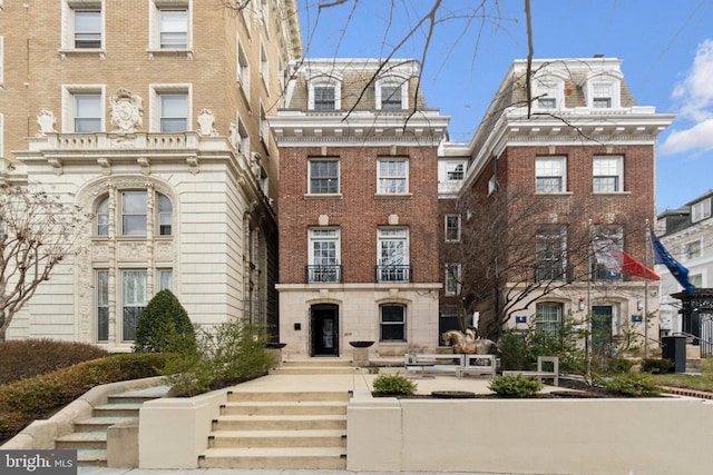 view of front facade featuring brick siding, a high end roof, and mansard roof