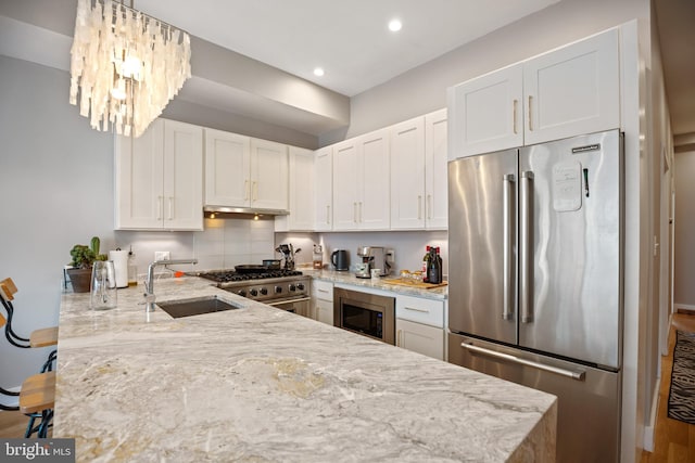 kitchen with a peninsula, light stone countertops, white cabinetry, and premium appliances