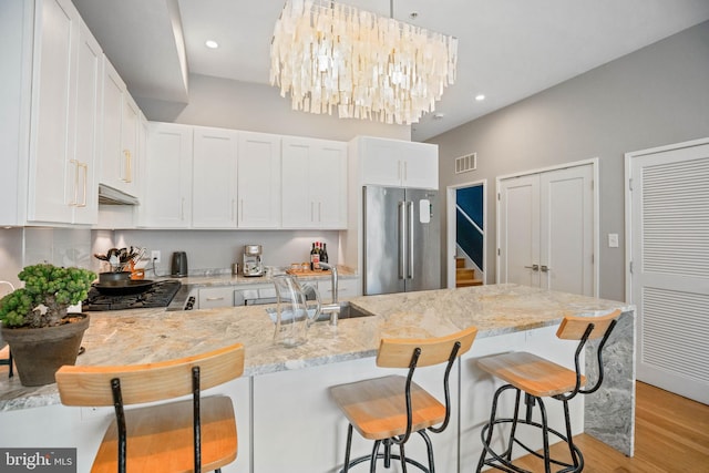 kitchen featuring appliances with stainless steel finishes, white cabinets, a sink, and light stone countertops