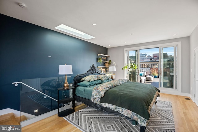 bedroom featuring access to exterior, a skylight, recessed lighting, and wood finished floors