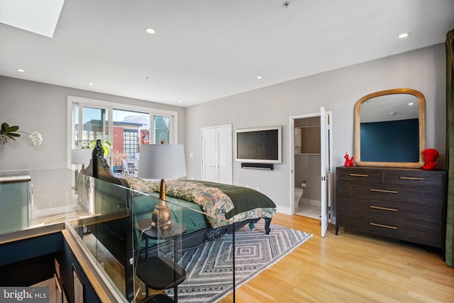 bedroom featuring light wood finished floors, a skylight, ensuite bathroom, and recessed lighting