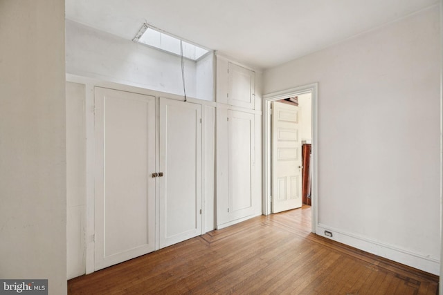 unfurnished bedroom with a skylight, baseboards, and hardwood / wood-style floors