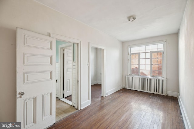 empty room featuring hardwood / wood-style flooring, radiator heating unit, and baseboards