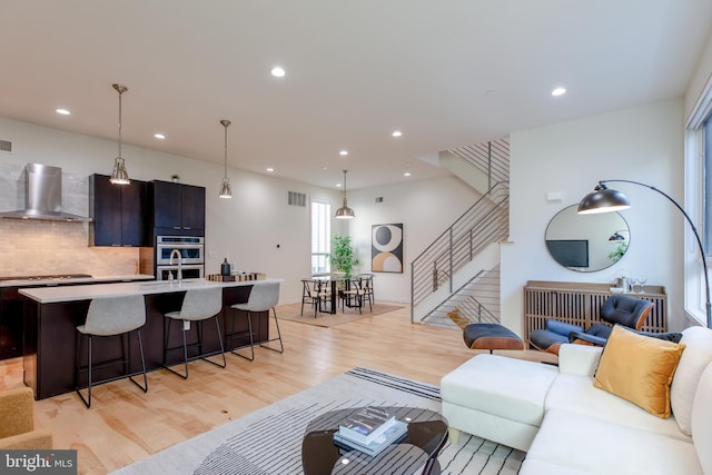 living room with light wood-type flooring, visible vents, stairway, and recessed lighting