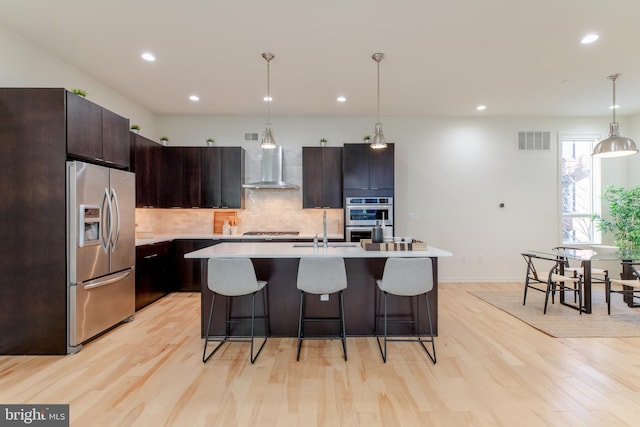 kitchen with stainless steel appliances, visible vents, light countertops, wall chimney exhaust hood, and decorative light fixtures