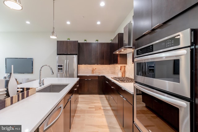 kitchen with wall chimney exhaust hood, appliances with stainless steel finishes, hanging light fixtures, light countertops, and a sink