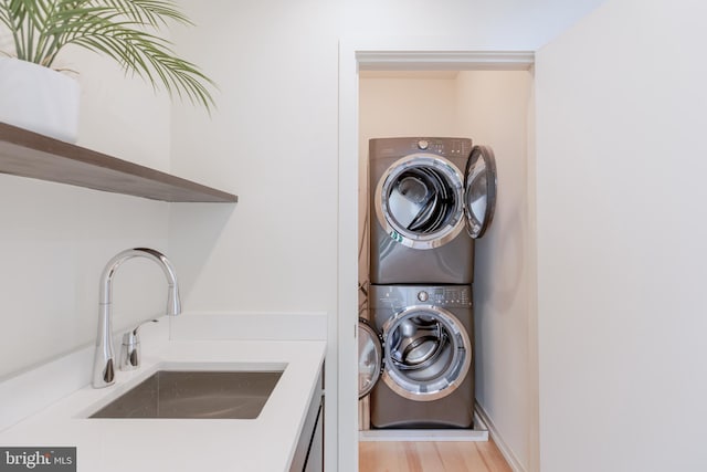 clothes washing area with laundry area, a sink, light wood-style flooring, and stacked washing maching and dryer