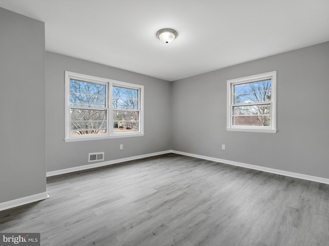 spare room featuring wood finished floors, visible vents, and baseboards