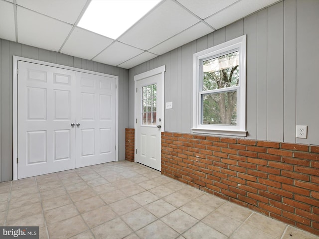 foyer with brick wall, a drop ceiling, and light tile patterned flooring