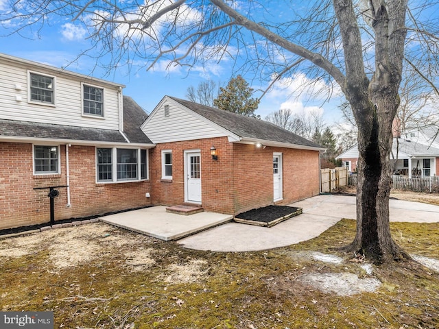 rear view of property featuring a shingled roof, fence, a patio, and brick siding