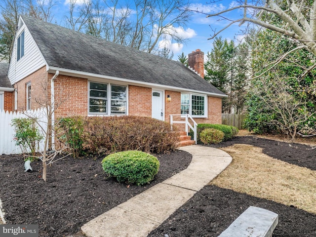 view of front facade featuring a shingled roof, brick siding, fence, and a chimney