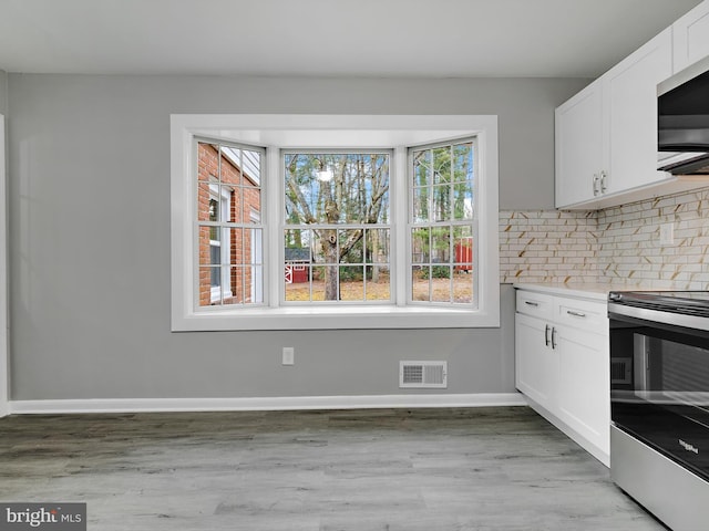 kitchen featuring stainless steel appliances, visible vents, baseboards, white cabinetry, and backsplash