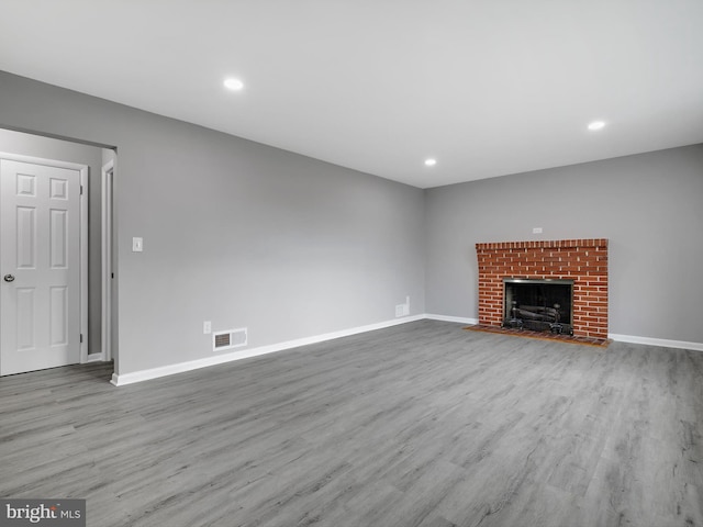 unfurnished living room featuring baseboards, visible vents, wood finished floors, a brick fireplace, and recessed lighting