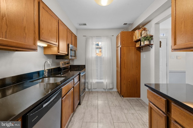 kitchen with visible vents, appliances with stainless steel finishes, brown cabinetry, a sink, and dark stone counters