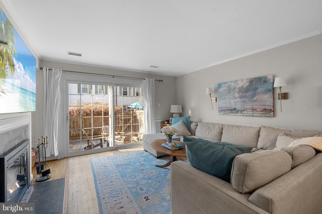 living room with hardwood / wood-style floors, a fireplace with flush hearth, visible vents, and crown molding