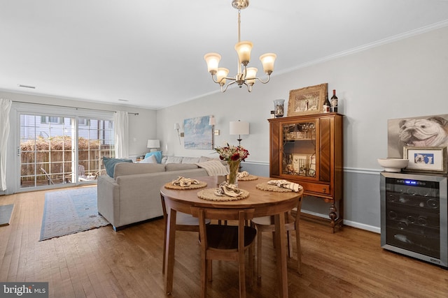 dining room featuring hardwood / wood-style flooring, a notable chandelier, wine cooler, and crown molding