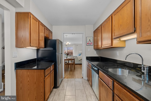 kitchen with a notable chandelier, a sink, appliances with stainless steel finishes, brown cabinetry, and dark stone countertops