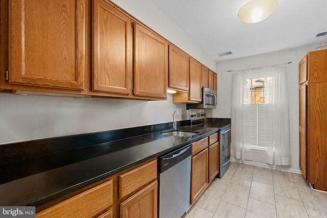 kitchen featuring light tile patterned floors, a sink, visible vents, appliances with stainless steel finishes, and brown cabinetry