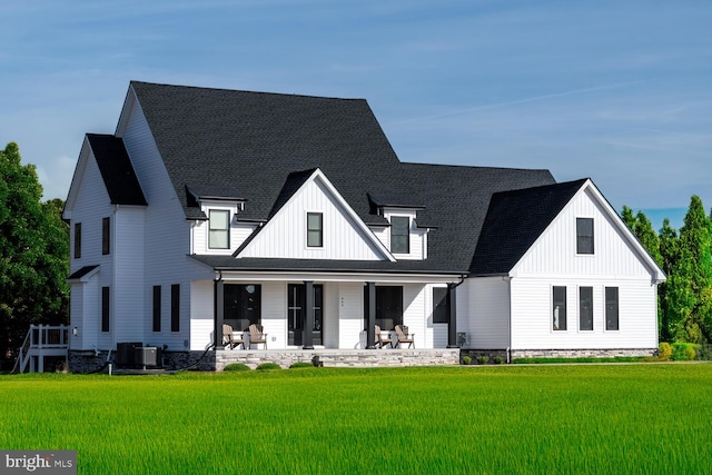 view of front of house featuring roof with shingles, covered porch, cooling unit, board and batten siding, and a front yard