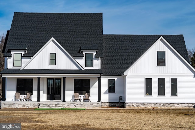 back of property featuring a shingled roof, covered porch, and a yard