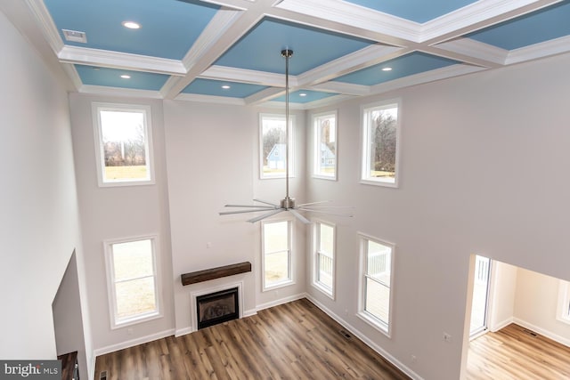unfurnished living room with a fireplace, wood finished floors, coffered ceiling, a wealth of natural light, and beamed ceiling