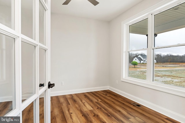 empty room featuring visible vents, dark wood-type flooring, a ceiling fan, and baseboards