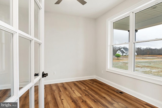 empty room with dark wood-style floors, a ceiling fan, visible vents, and baseboards