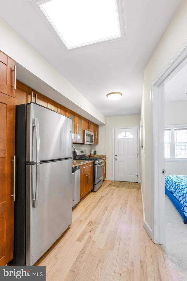 kitchen with baseboards, light wood-style floors, appliances with stainless steel finishes, brown cabinets, and dark countertops