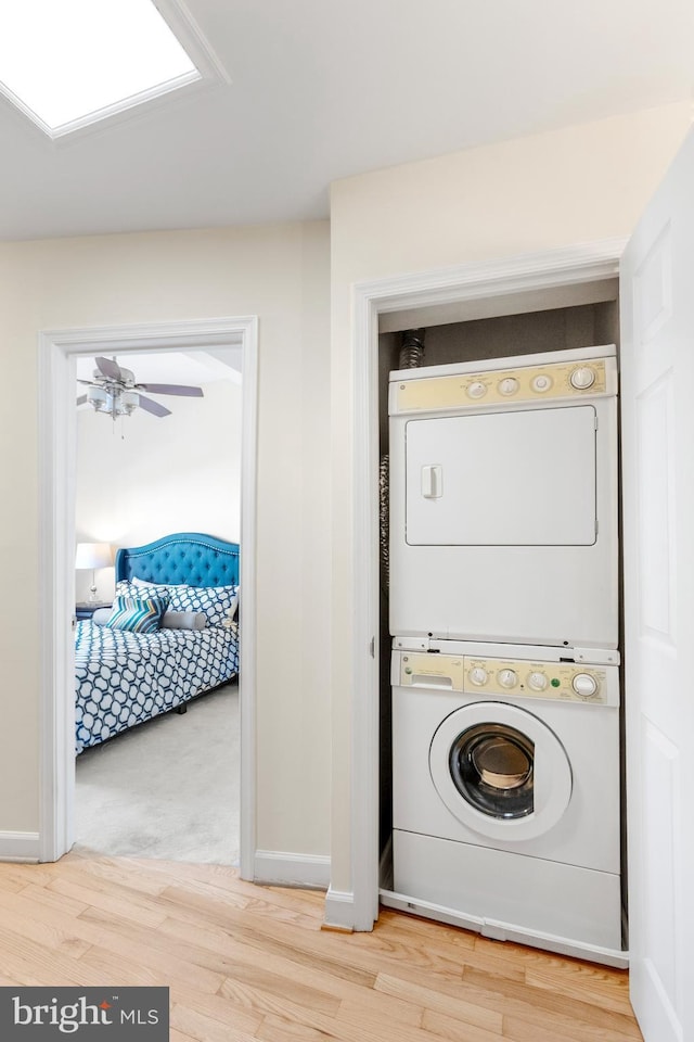 clothes washing area with ceiling fan, stacked washing maching and dryer, wood finished floors, and baseboards