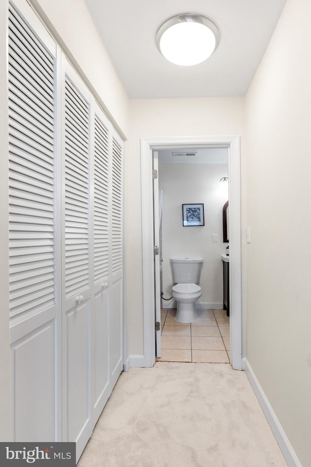 hall with light carpet, baseboards, visible vents, and light tile patterned flooring