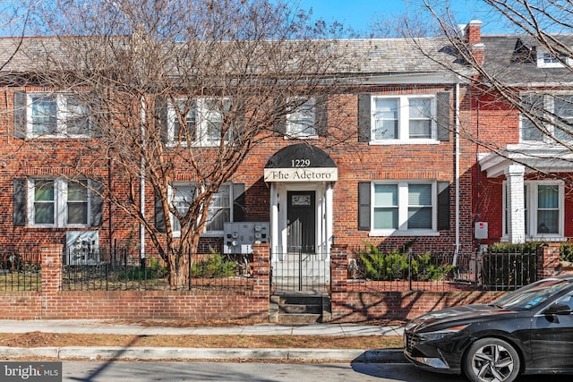 view of property featuring a fenced front yard, a high end roof, and brick siding