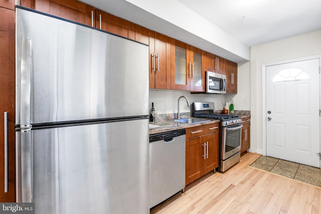 kitchen featuring brown cabinets, stainless steel appliances, glass insert cabinets, a sink, and light wood-type flooring