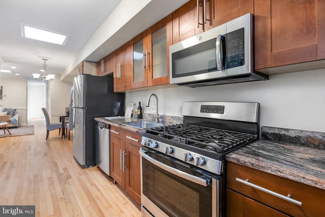 kitchen with stainless steel appliances, brown cabinetry, a sink, and light wood-style floors