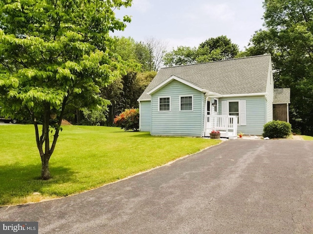 view of front facade with aphalt driveway, a front yard, and roof with shingles