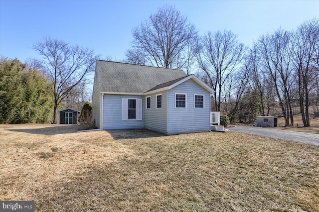 exterior space with a shingled roof, an outbuilding, a lawn, and a storage unit